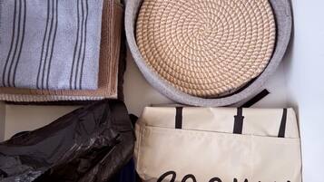 A storage box containing various items including a woven basket, a striped fabric, a black plastic bag, a beige bag with 'COOKIN' text, and a woven tray.