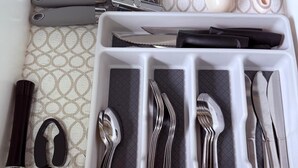 A kitchen drawer with utensils organized in compartments, including knives, spoons, and a grater.