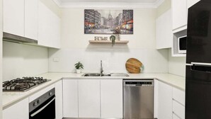 A modern kitchen with white cabinets, a gas stove, a dishwasher, and a painting of a cityscape above the sink.