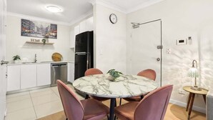 A modern kitchen with white cabinets, a black refrigerator, a dining table with pink chairs, and a clock on the wall.