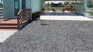 Un edificio de dos plantas con un balcón, un patio cubierto y un camino de entrada de grava.