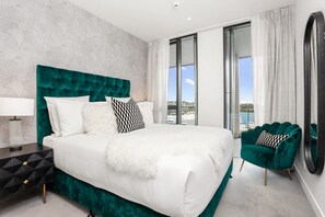 Ein modernes Hotelzimmer mit einem großen Bett, einem Nachttisch, einem grünen Sessel und Meerblick.