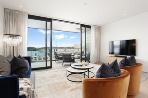 Un salon moderne doté d’un grand téléviseur, de sièges confortables, d’un balcon offrant une vue sur le port de plaisance et d’un lustre.