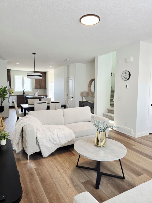 A modern living room with a sectional sofa, a round coffee table, and a kitchen in the background. - Bright & Homey 3br New Home in NW Calgary (Calgary)