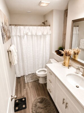 Un baño moderno con cortina de ducha, inodoro, lavamanos y espejo.