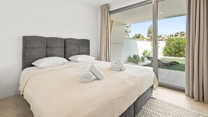 Een slaapkamer met een groot bed, een schuifglasdeur naar een balkon en uitzicht op de omgeving.