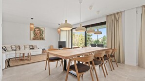 Een eetgedeelte met een houten tafel en stoelen, een bank en hanglampen.