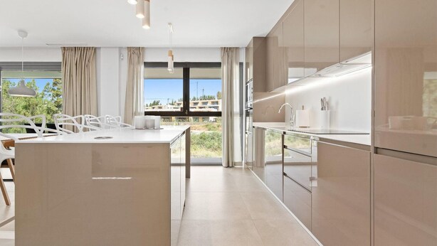 Een moderne keuken met een centraal eiland, grote ramen en uitzicht op gebouwen.