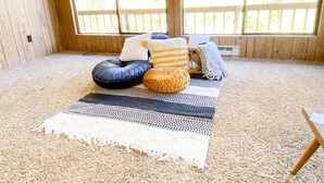 A room with a large window, a carpeted floor, and a bed with pillows and a blanket.