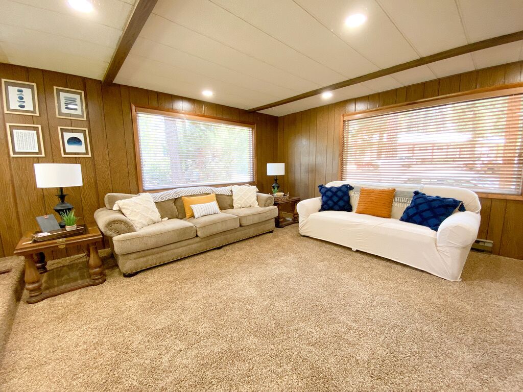 A living room with two sofas, wooden paneled walls, framed pictures, and a carpeted floor.