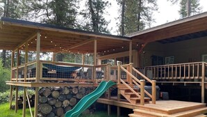 A wooden deck with a slide, steps, and a covered area with string lights.