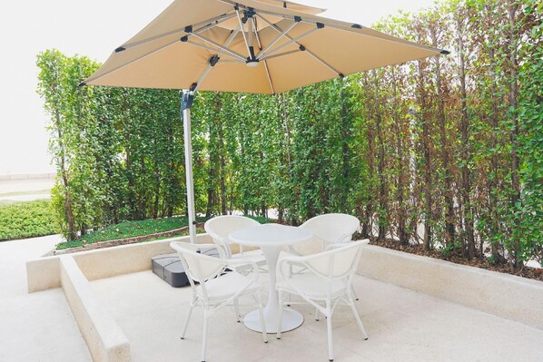 A patio area with a table and chairs, a beige umbrella, and a hedge in the background. - Novotel Chongqing Airport (Chongqing)