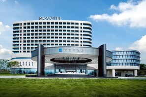 A modern hotel with a curved facade, a prominent entrance, and a clear sky. - Novotel Chongqing Airport (Chongqing)