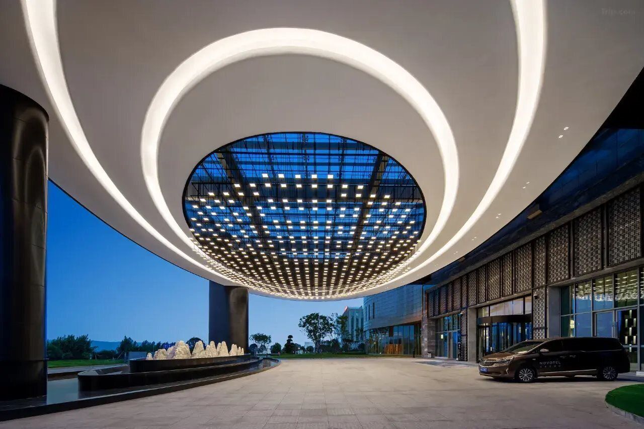 Entrada de hotel moderna con un tragaluz circular, un coche estacionado fuera y cielo despejado.