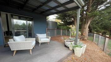 A covered patio with wicker furniture, a large planter, and a tree.