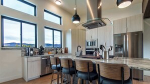 A modern kitchen with a large island, bar stools, and a view of the mountains. - Teton Homestead: Shambala Private Mountain Retreat (Victor)
