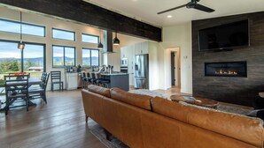 A spacious living area with a leather sofa, a dining table with chairs, a kitchen area with modern appliances, and a fireplace. - Teton Homestead: Shambala Private Mountain Retreat (Victor)