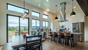 A modern kitchen with large windows, a dining area, and a bar. - Teton Homestead: Shambala Private Mountain Retreat (Victor)