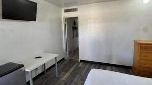 Una habitación con cama, escritorio, televisor y armario.