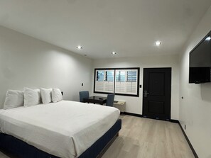 A bedroom with a large bed, a desk with a chair, a door, and a mounted TV.