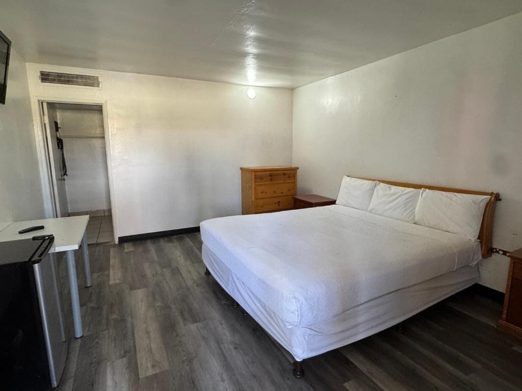 Een slaapkamer met een bed, een houten dressoir, een bureau en een deur.