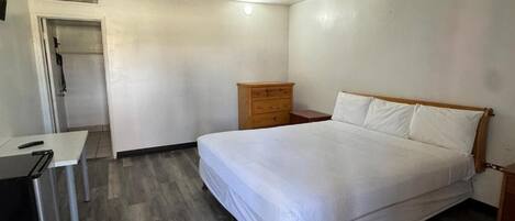 Um quarto com cama, cómoda de madeira, escrivaninha e porta.