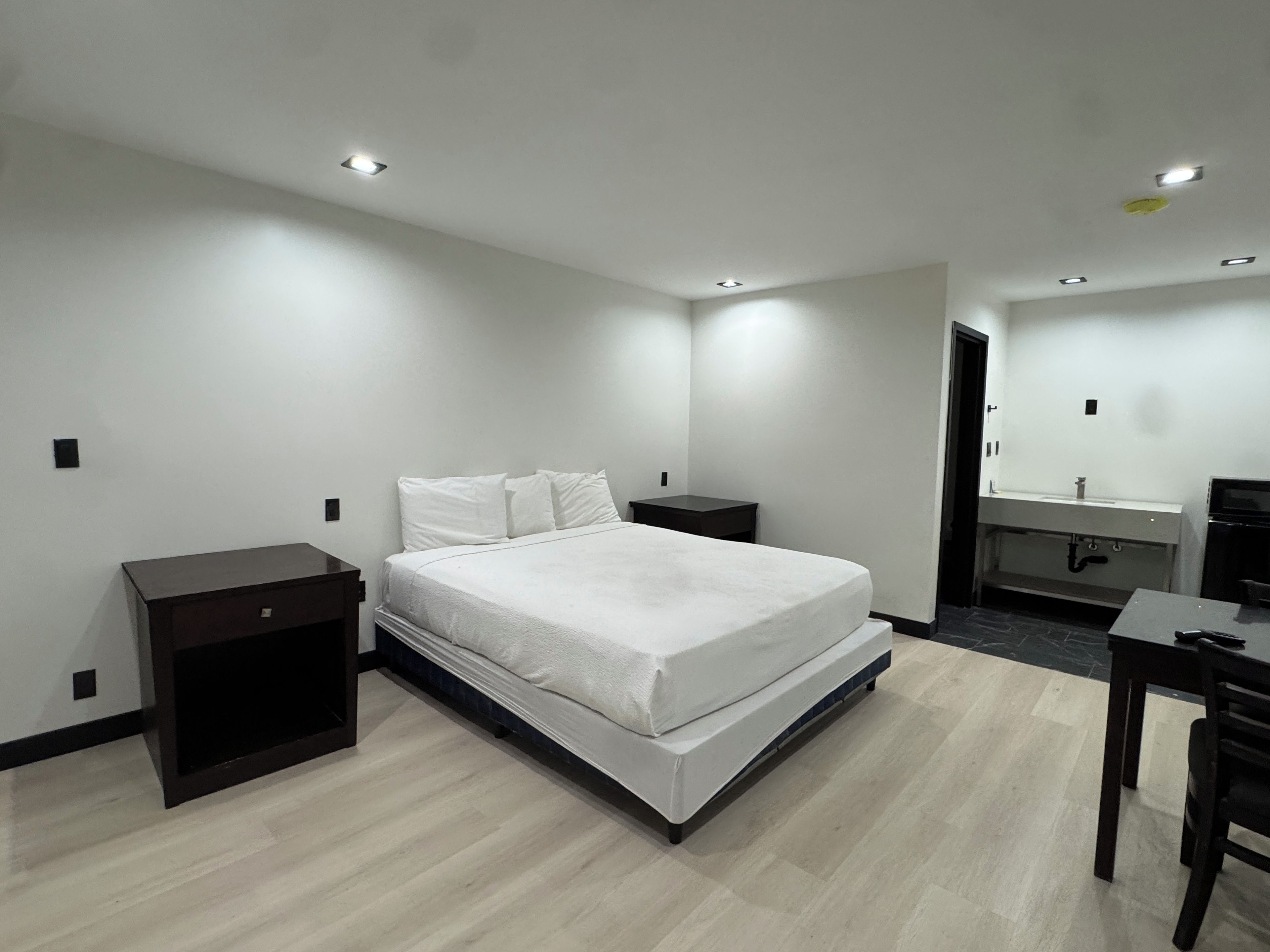 A modern bedroom with a bed, bedside tables, a desk, and a bathroom with a mirror and sink.