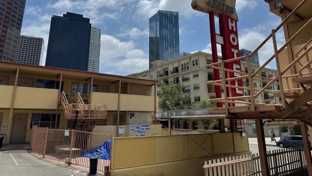 Un hotel con un letrero rojo llamativo, una escalera y vistas de edificios altos circundantes.