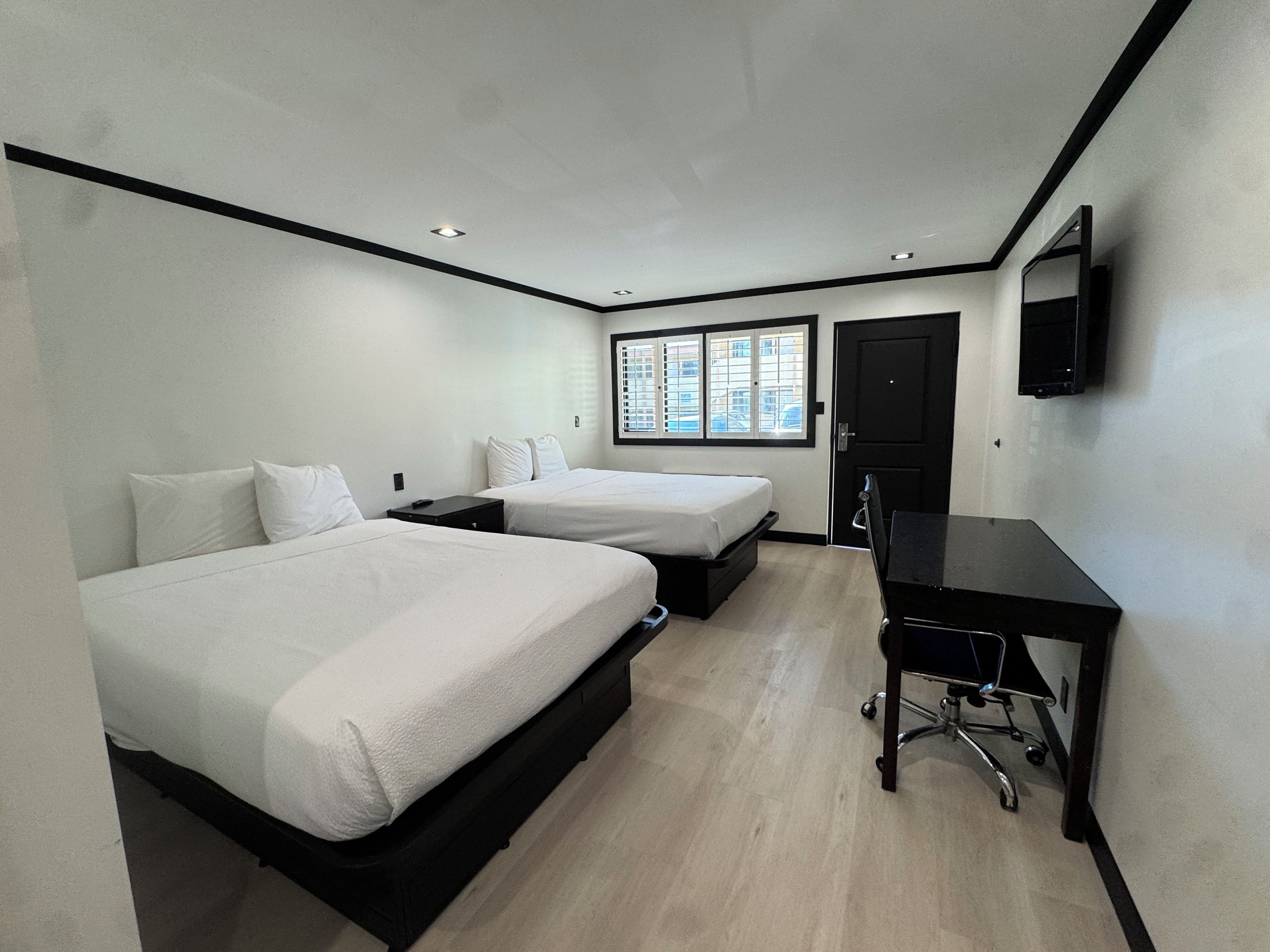 A hotel room with two beds, a desk, a chair, a TV, and a window with blinds.