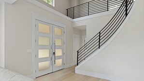 Amplio interior con una escalera curva, una puerta blanca con paneles de vidrio y un piso de color claro.
