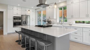 Una cocina moderna con armarios blancos, electrodomésticos de acero inoxidable, una isla grande con taburetes altos e iluminación colgante.