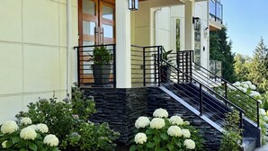 Una casa moderna de dos pisos con un porche cubierto, una escalera de piedra y un jardín bien cuidado con hortensias.