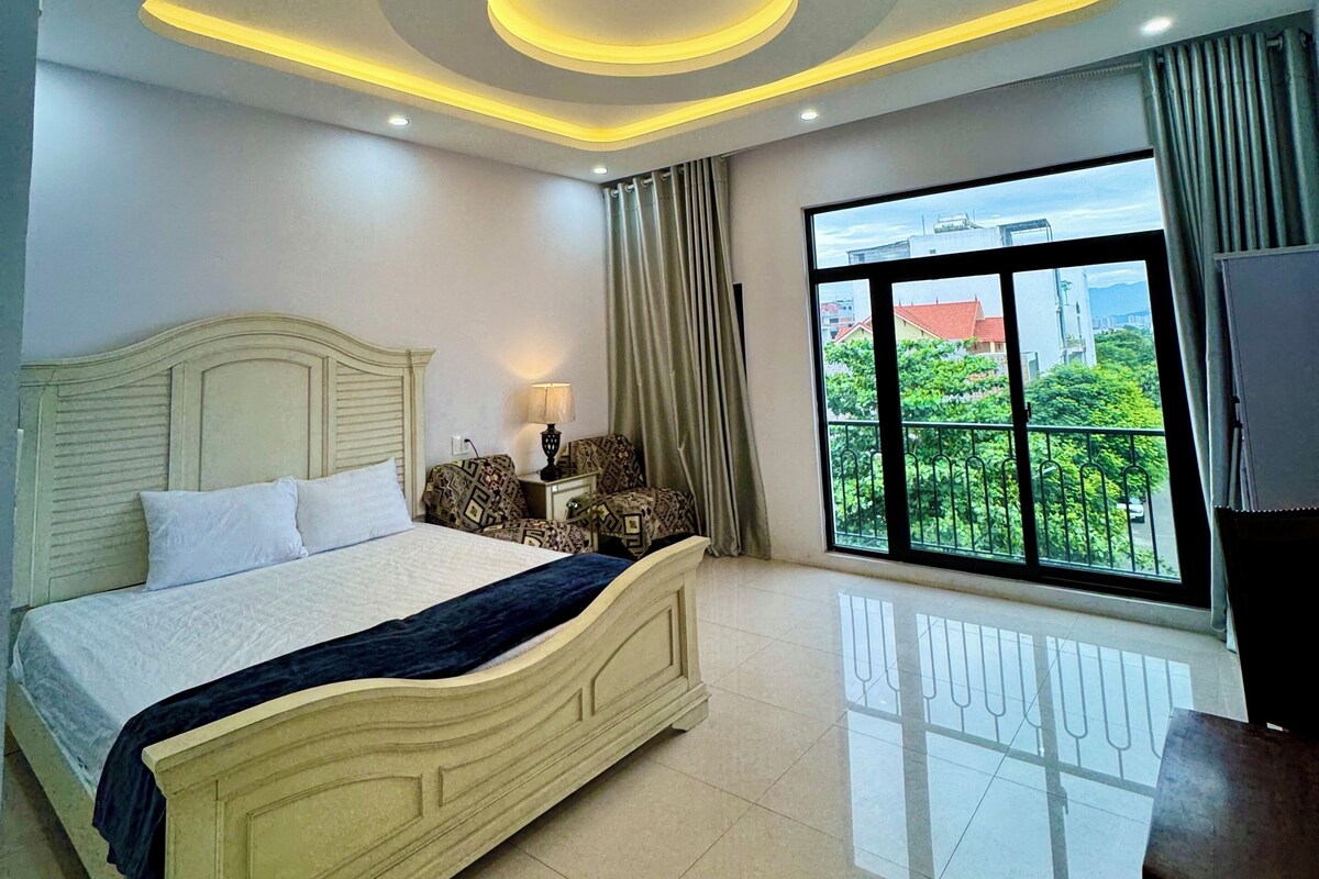 Une chambre moderne avec un grand lit, un luminaire au plafond et une vue sur la verdure.