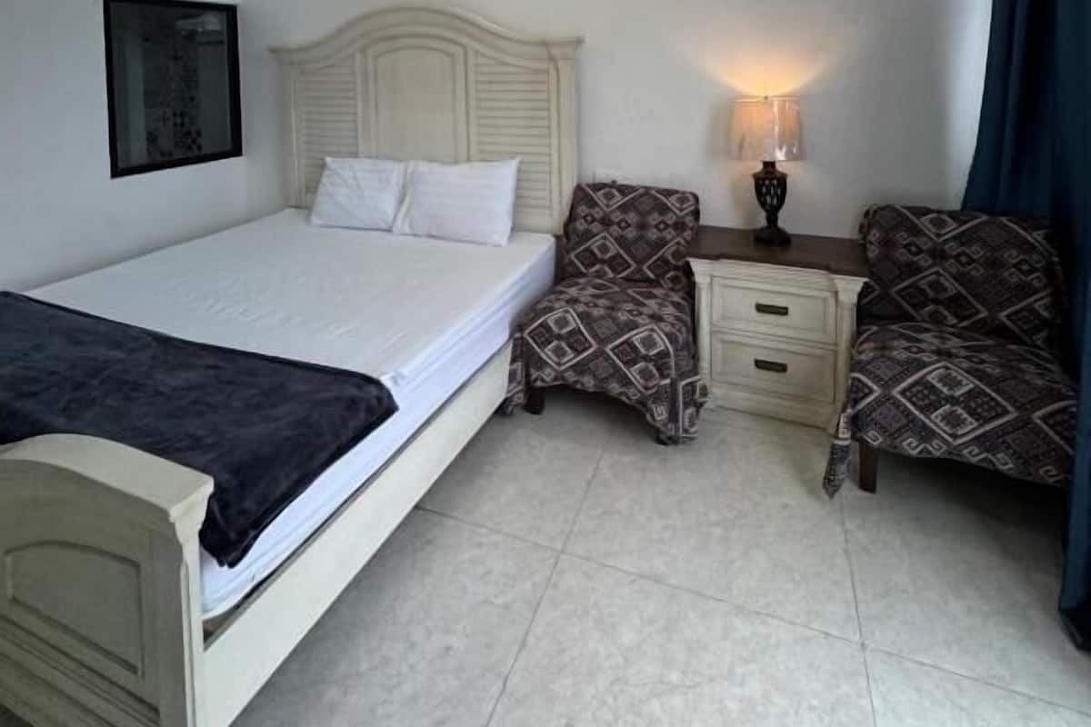 Un dormitorio con cama, mesitas de noche, lámpara y sillas estampadas.