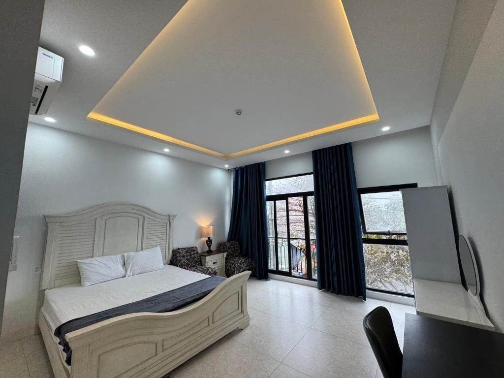 A modern bedroom with a bed, bedside table, lamp, and a view through a large window.