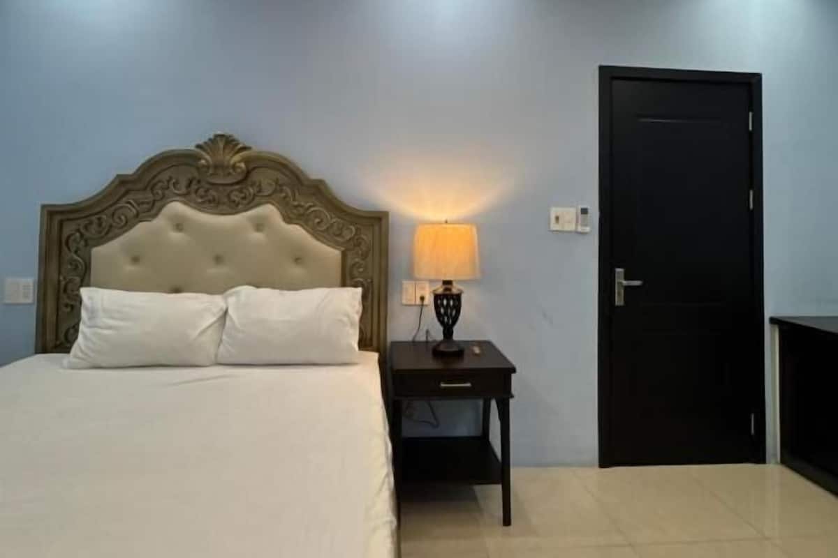 Un dormitorio con cama, mesita de noche, lámpara y puerta.