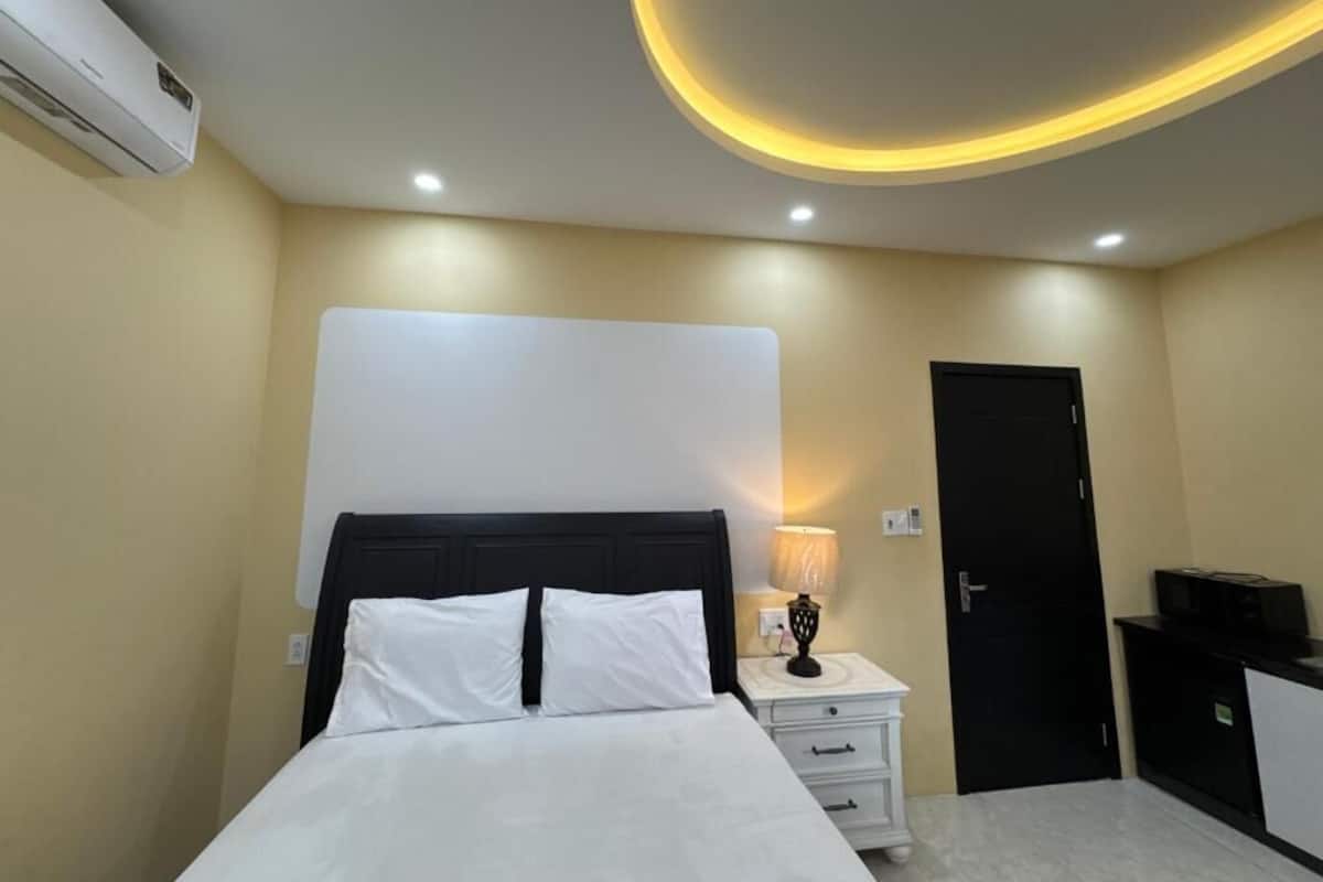 Una habitación de hotel con cama, mesita de noche, lámpara, aire acondicionado y una puerta.