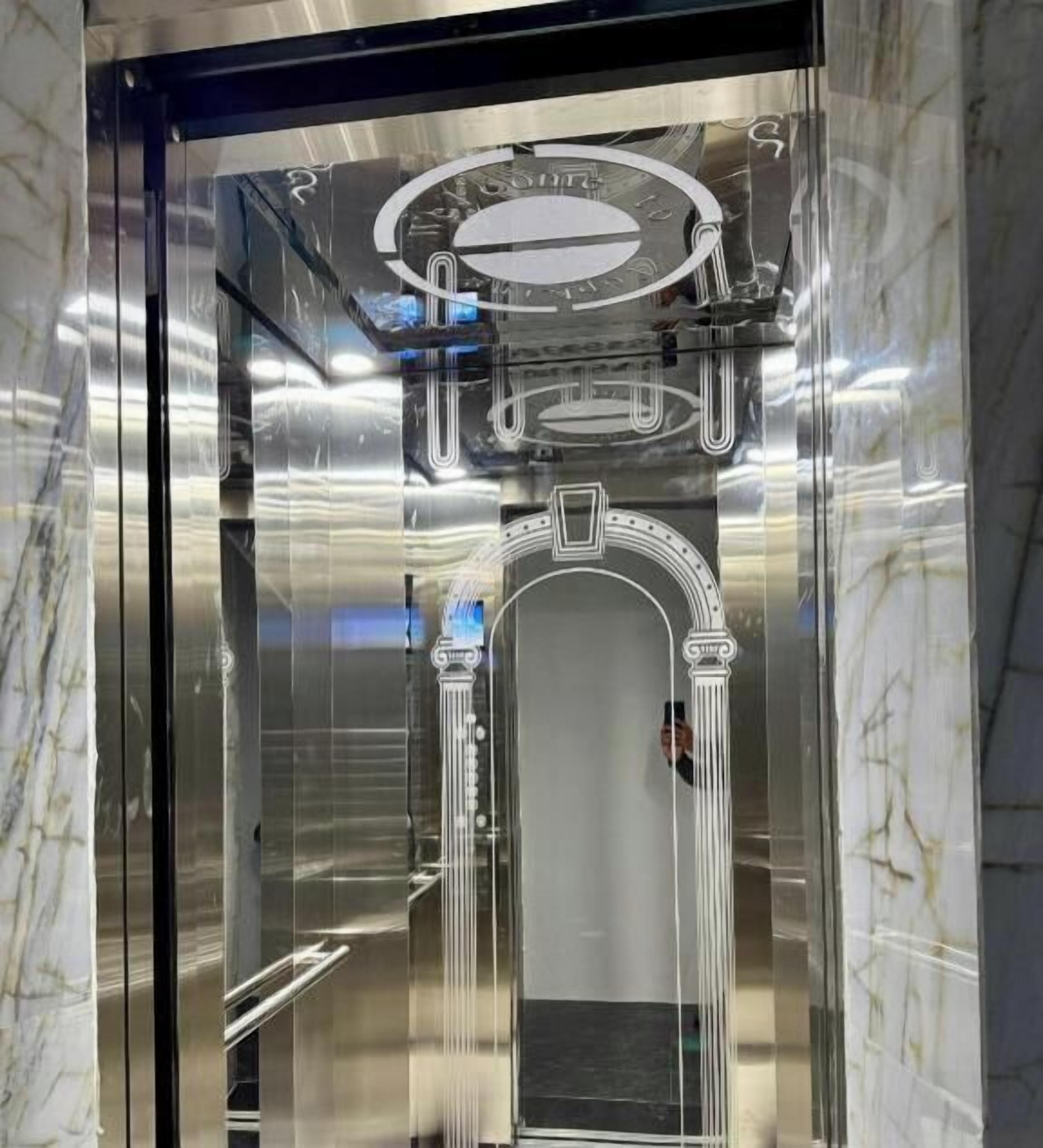 An elevator interior with a marble wall, a metallic handrail, and a circular control panel.