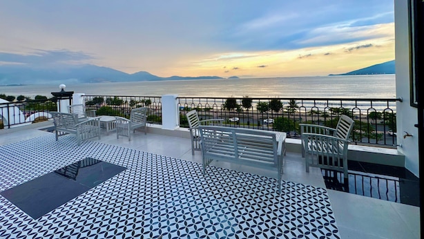 A terrace with a patterned floor, outdoor seating, and a view of the sea and mountains.