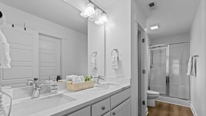 A modern bathroom with a large mirror, dual sinks, a shower, and a wooden floor. - Modern Charlotte Retreat Near Uptown (Charlotte)