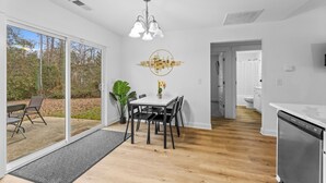 A modern kitchen with a dishwasher, a dining area with a table and chairs, and a large sliding glass door leading to a patio. - Modern Charlotte Retreat Near Uptown (Charlotte)