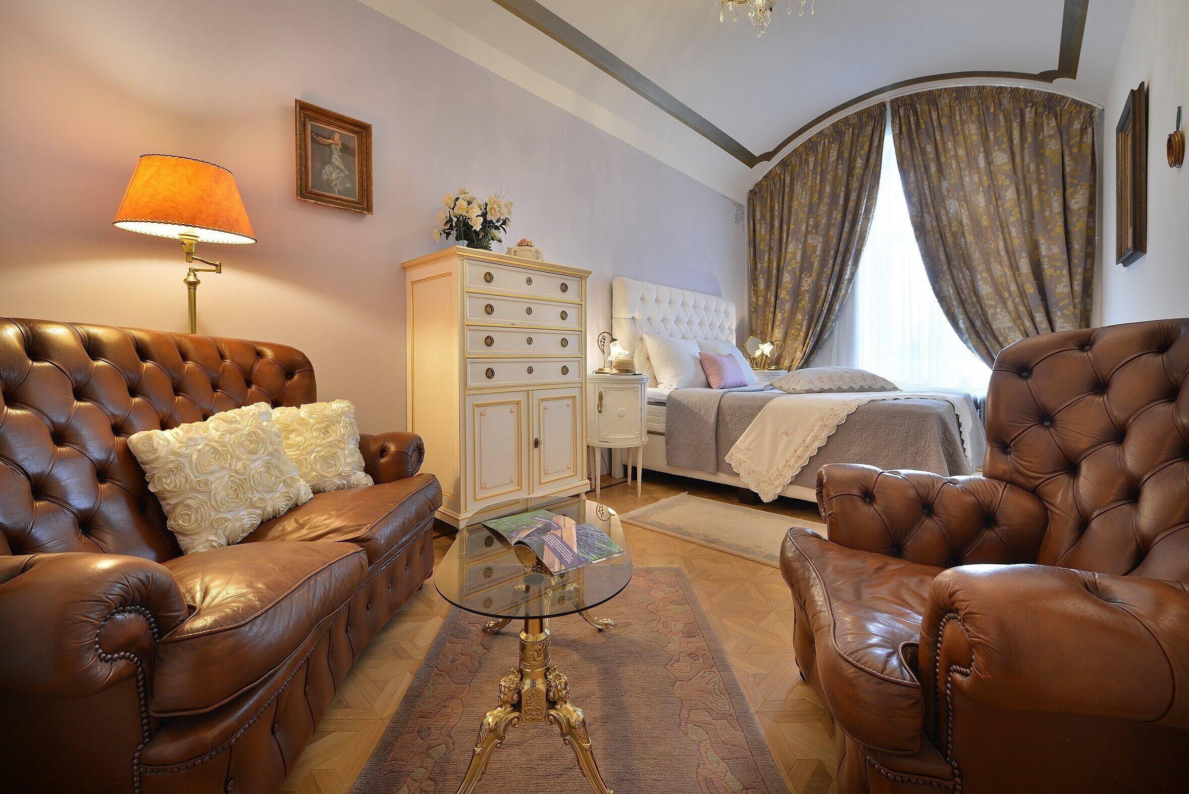 Ein Zimmer mit einem Bett, zwei Ledersofas, einem Glastisch, einem Nachttisch, einer Lampe und einer Kommode.