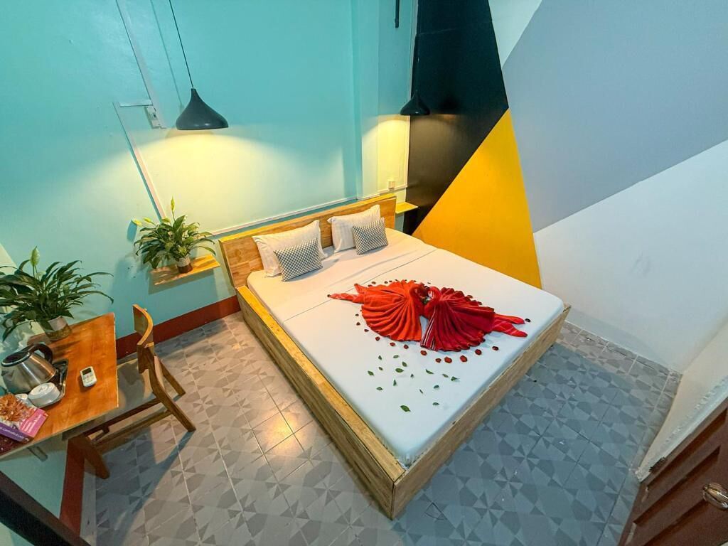 A hotel room with a bed, bedside table, chair, and potted plants.