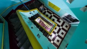 A high-angle view of a hotel lobby with a checkered floor pattern, a staircase, and a blue wall with rectangular windows. - Social Backpacker Hostel & Rooftop Bar (Battambang)