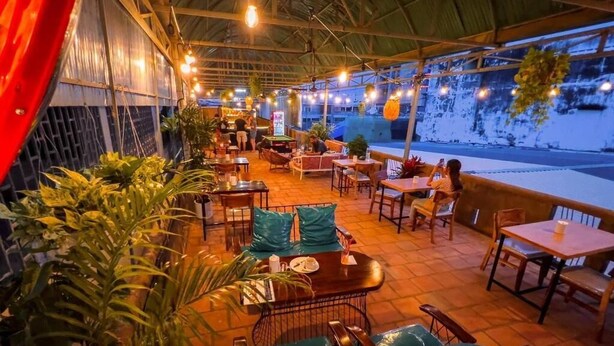 An outdoor restaurant with tables and chairs, surrounded by potted plants. - Social Backpacker Hostel & Rooftop Bar (Battambang)