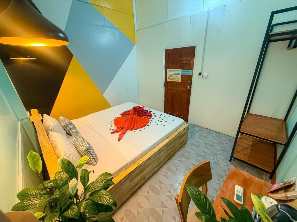 Een kleine, verzorgde kamer met een bed, nachtkastje, stoel en een lamp.