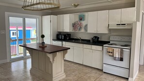 Une cuisine avec des meubles blancs, un îlot central, une cuisinière et un luminaire suspendu.