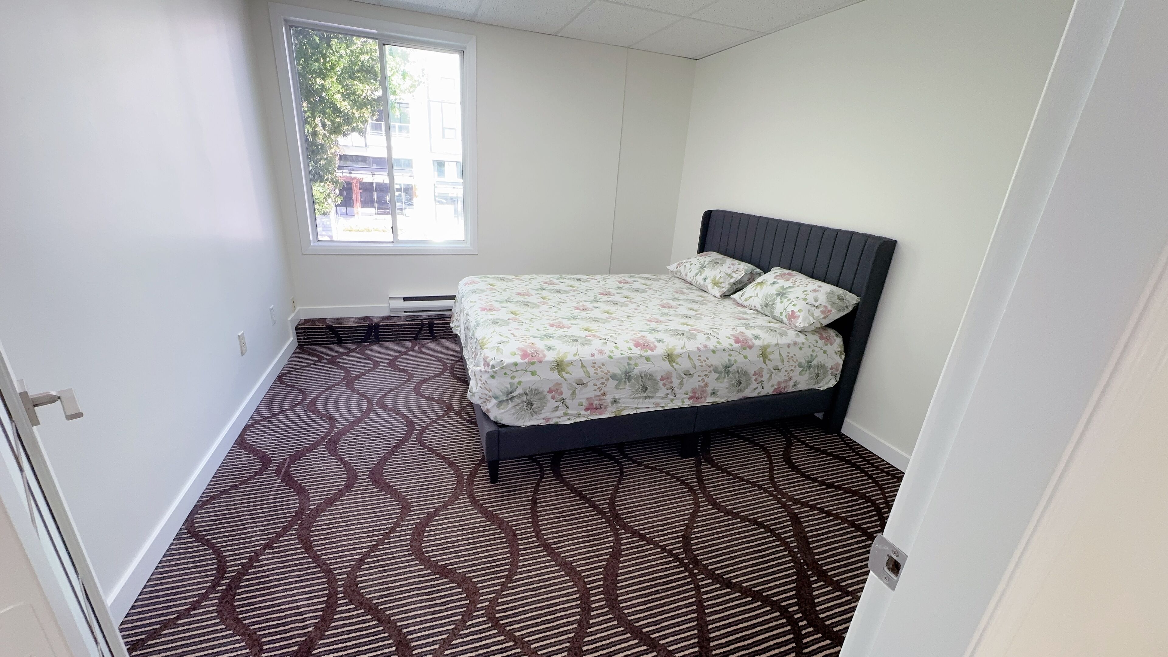 Ein kleines Schlafzimmer mit einem Bett, einem Fenster und einem gemusterten Teppich.