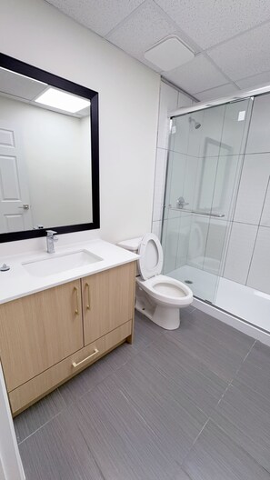 Een moderne badkamer met een wit wastafelmeubel, spiegel en toilet, plus een douchecabine met glazen wanden.