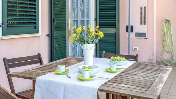 A table set with a white tablecloth, green plates, and a vase of yellow flowers. - Italian Experience- Sweet Loreto (Loreto)